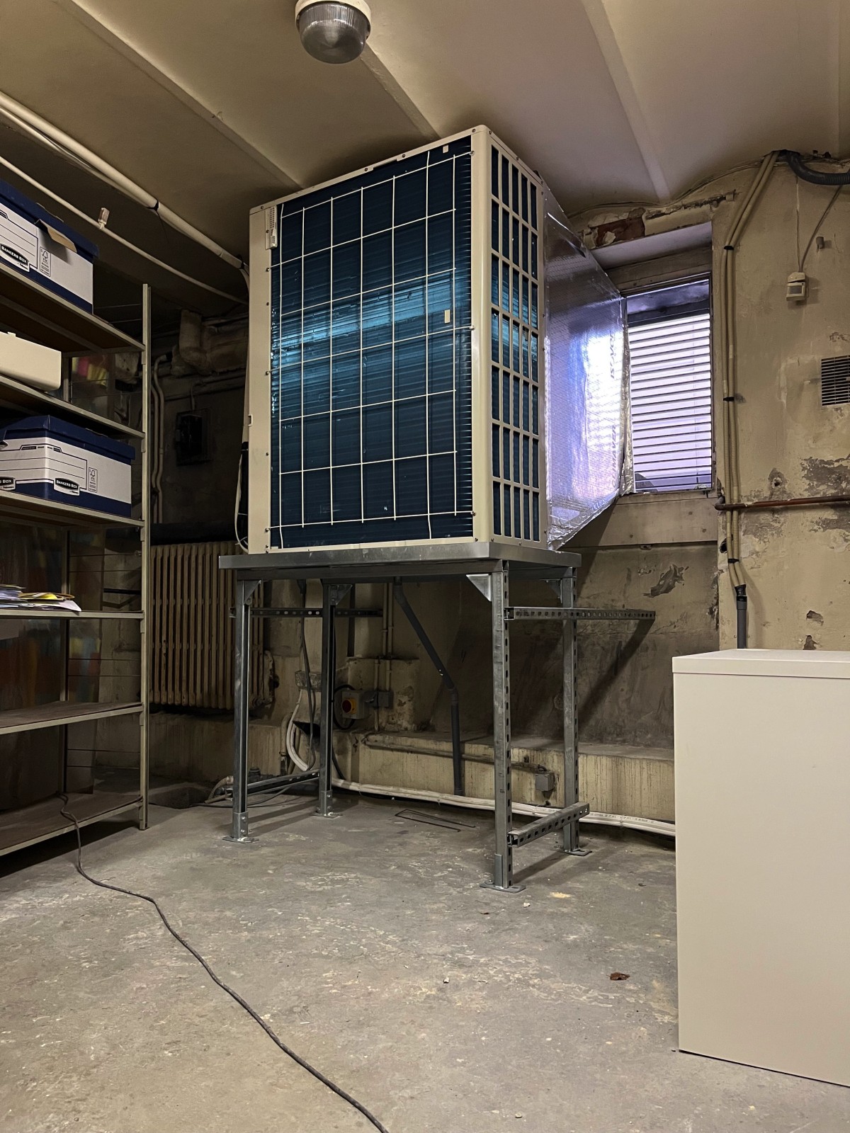 Groupe extérieur VRF General installé dans une cave derrière une trappe à charbon à Bordeaux